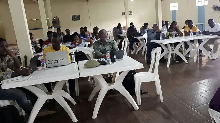 Men and women sit inside at tables writing and discussing with one another.