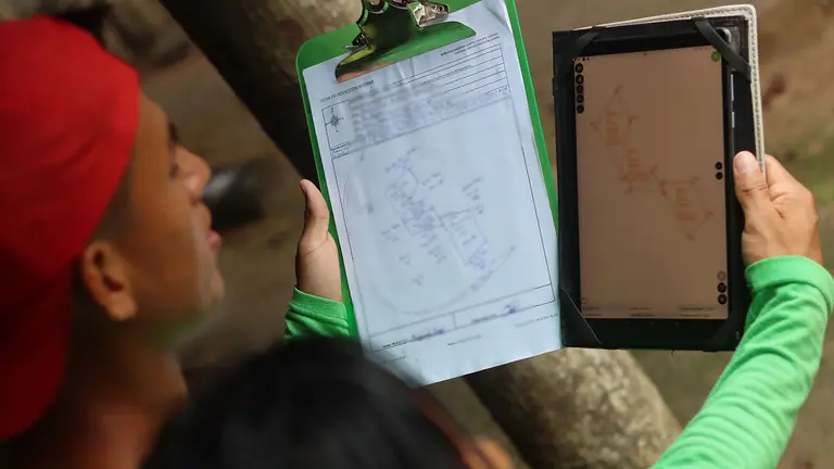 Two people look at a clipboard and an electronic tablet held up alongside one another.