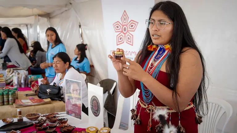 A woman stands behind a stall showing off a small pot. 