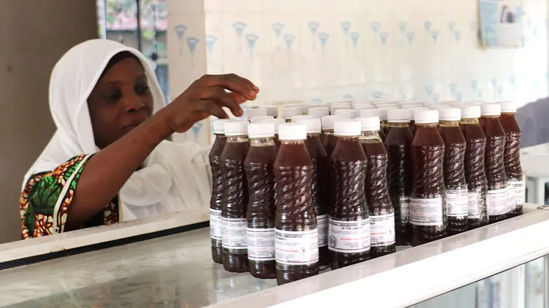 A woman reaches up to a shelf on which are stacked bottles of honey.