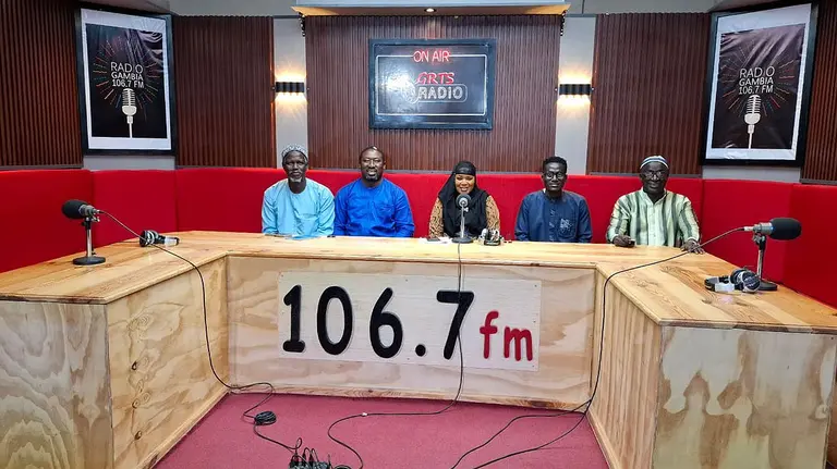 Four people sit behind a desk, on which sit microphones. "106.7fm" is written on the front of the desk.