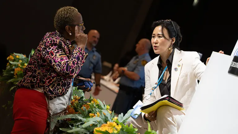 Two people with lanyards hanging from their necks engage in a discussion.