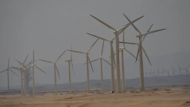 Wind turbines revolve under a blue sky.