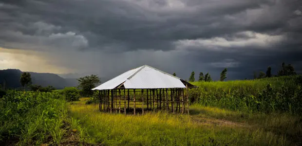 A church under construction sits on a verdant green field with dark grey storm clouds behind. 
