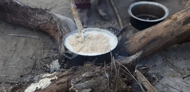 A pot with bubbling food sits cooking on an open fire.