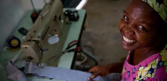 A smiling woman from Kenya sits beside her sewing machine. 