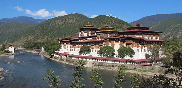 Picture of the Punakha Dzong, an administrative centre in Bhutan. A river runs past it in the foreground and wooded hills rise behind it.  