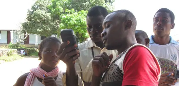 Young people in Okola, Cameroon, cluster around a Global Positioning System that they are using to create a community map with geographical features.