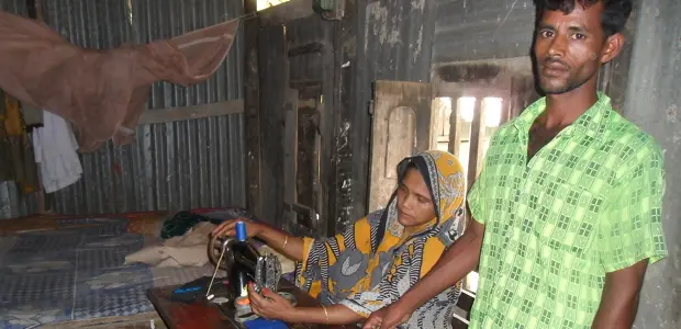 Bangladeshi man stands next to a woman who is working on a sewing machine