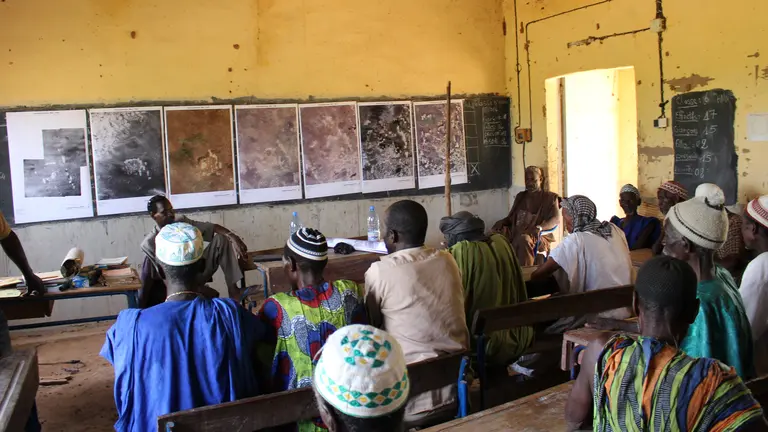 people sit as desks looking forward at photos pinned on a wall.