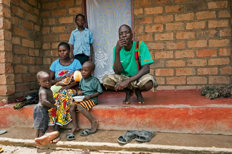 Andrew squats outside his brick home with his family.