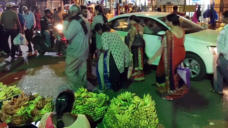 A street scene with pedestrians, stallholders, motorbikes and cars 
