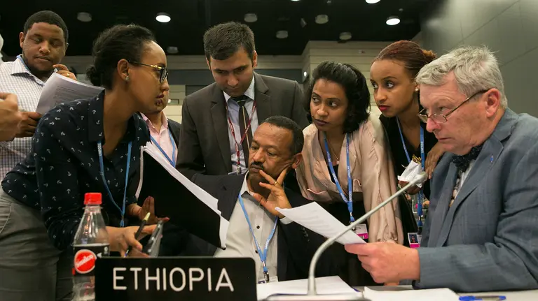 A huddle of people gather around one person to give advice and discuss negotiating tactics