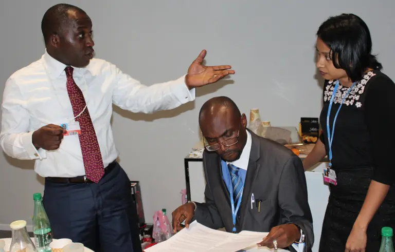 Three people gather to discuss a document one of them is holding in his hand