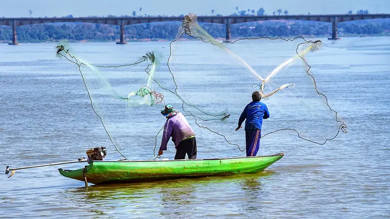 Two fishermen cast their nets from a small boat