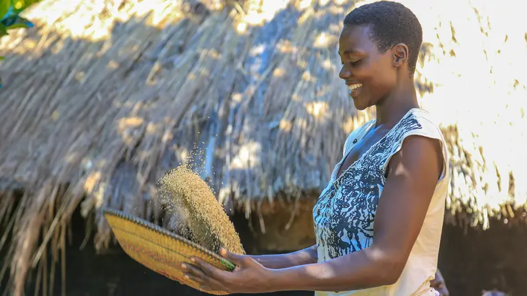 Evelyne  Flora Latabu shaking a bowl of grains.