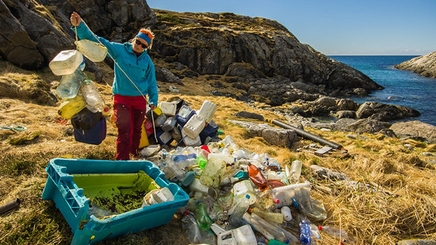 A beautiful coastline but, in the foreground, a woman is sorting a huge pile of plastic bottles