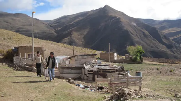 Two men stand in front of a building under construction, with mountains in the background