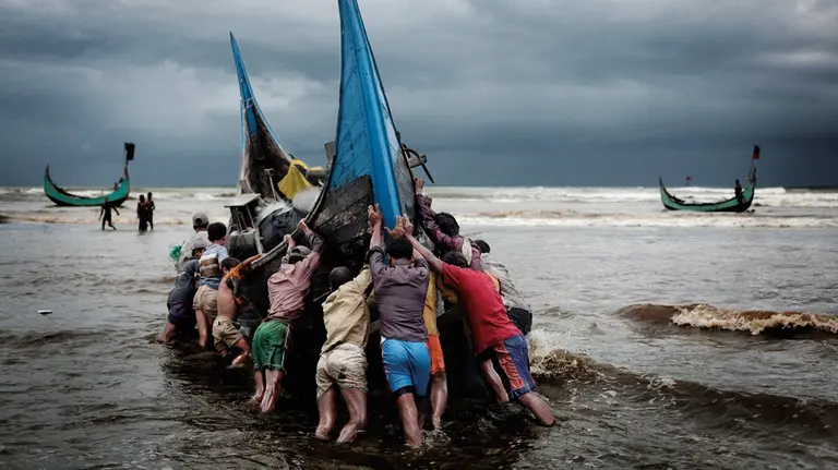 Group of fishers surround boat just offshore on a stormy day