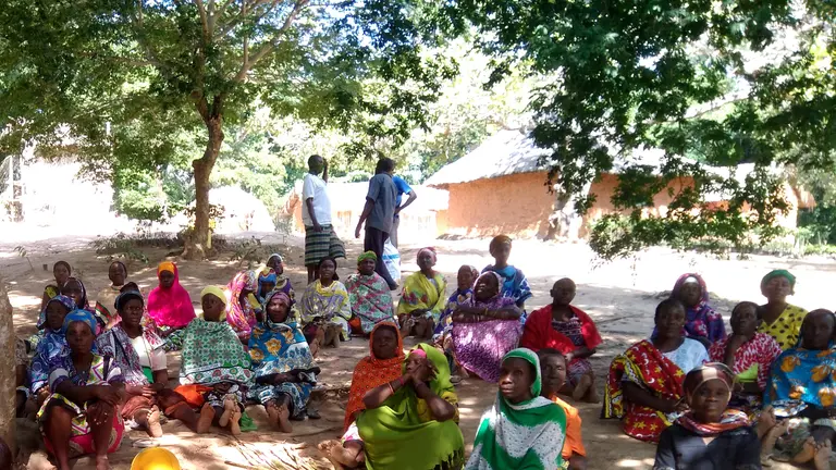 Women at an outside meeting sat on the floor under trees