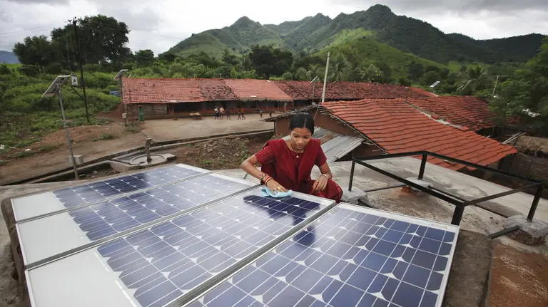 Indian woman does maintenance work on solar panel, with mountains in the background.