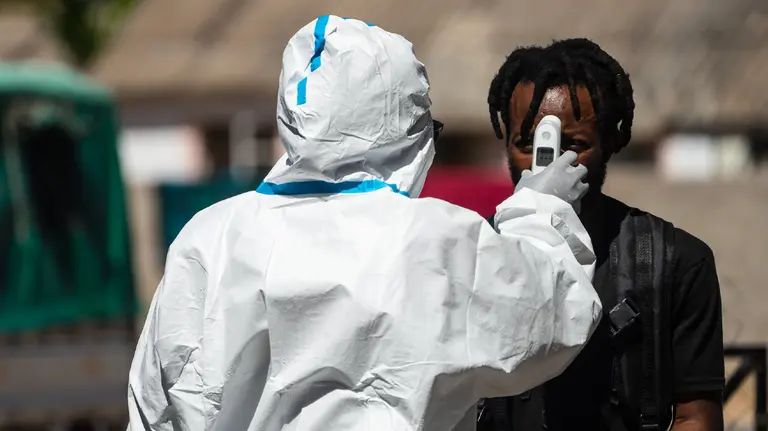 A man gets his temperature checked by someone in protective clothing.