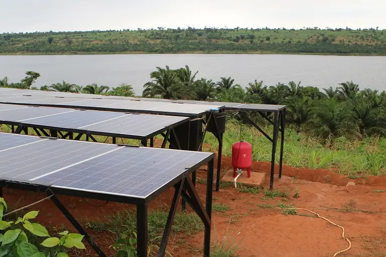 Solar panels on the ground next to a lake.