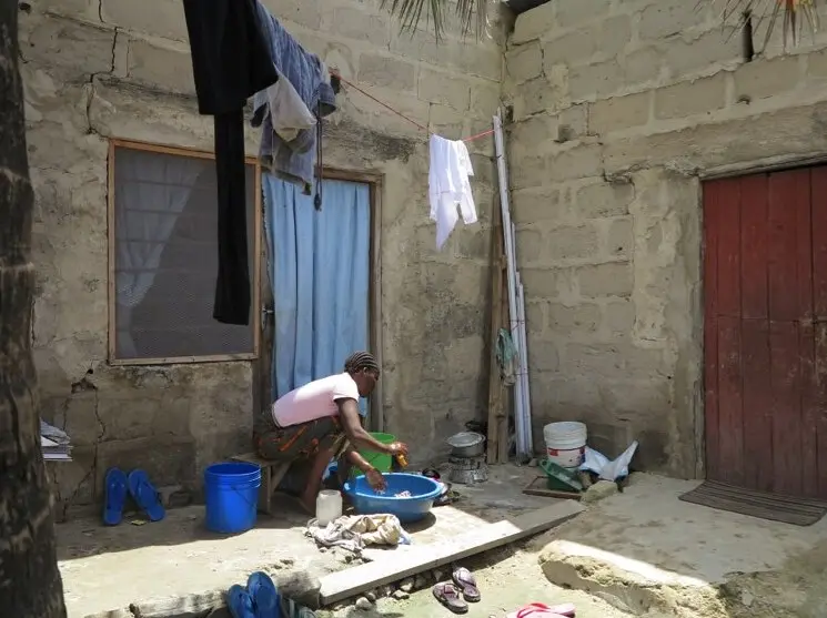 Woman washing dishes in a bowl outside.