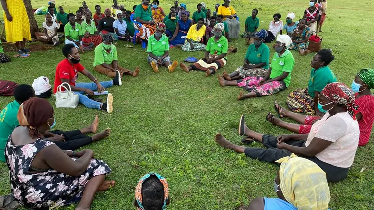 A group of people sit in a circle outside on grass. 
