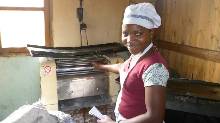 A woman wearing a chef's uniform and hat poses in front of a breadmaking machine