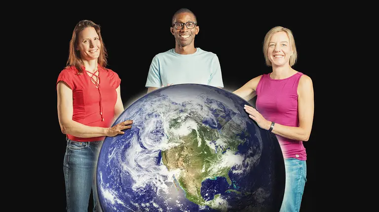 Three people stand around a large planet Earth globe  