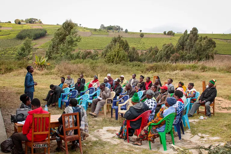 Group of people sitting outside in a semi-circle looking at someone presenting