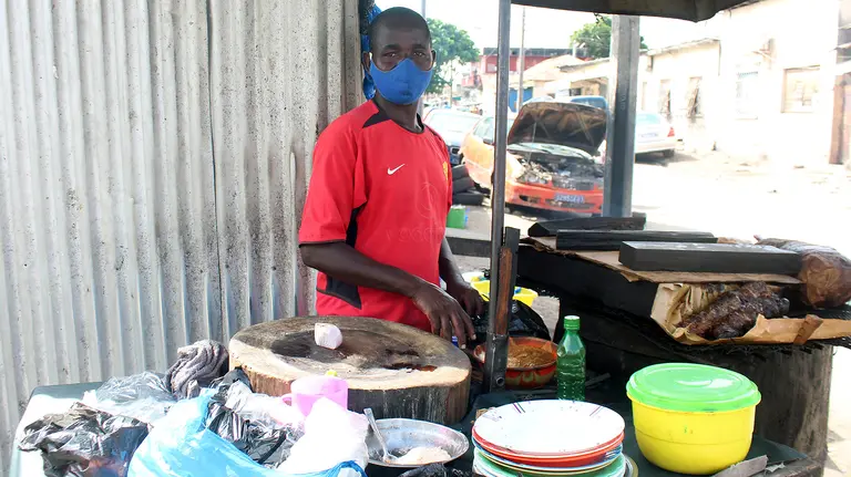 A mask-wearing man stands behind a food stall