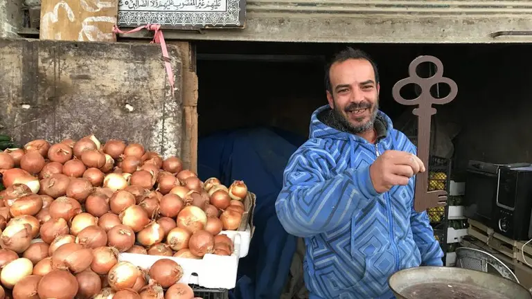 A man stands beside a tray of onions holding up an oversized symbolic key