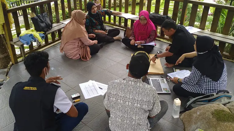 Men and women sit on the floor to talk with computers and paper in front of them 