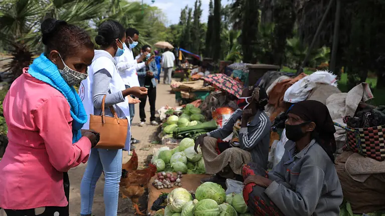 Women sit on the floor with lettuce on tables. Other women stand in front of them.