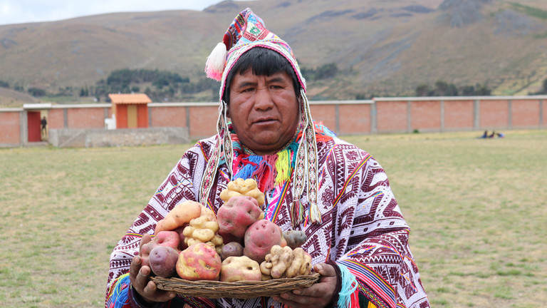 Man wearing traditional clothing holds a plate with potatoes.