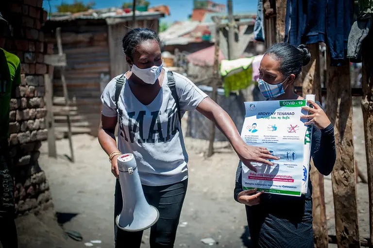 A woman holds a poster with instructions. Another one holds a loudpseaker and points at a poster.