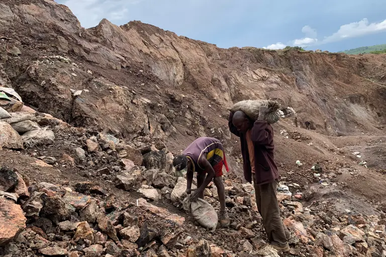 Two people carrying bags up a rocky incline