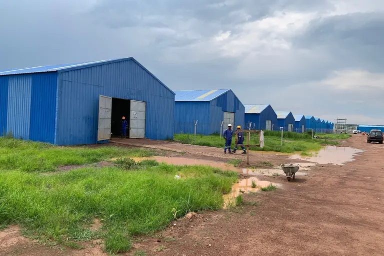 Men in overalls and hard hats outside a row of blue buildings