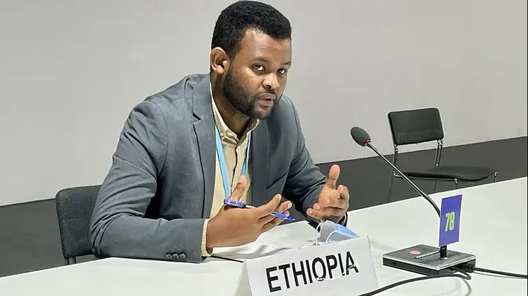 A man sat behind a desk and sign labelled 'Ethopia' gesticulates with his hands