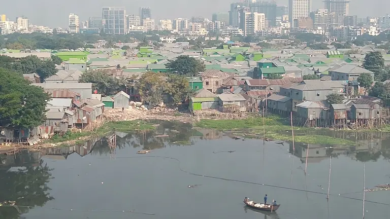 View of informal housing by a lake, with a boat in it. In the background modern buildings and skyscrapers
