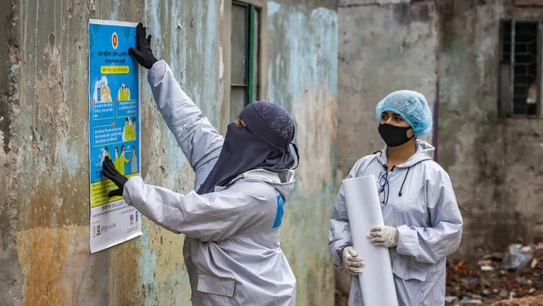 A woman puts up a poster while another looks on.