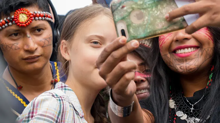 A close-up of a young girl, amid a crowd of people, looking at a mobile phone being held up for her