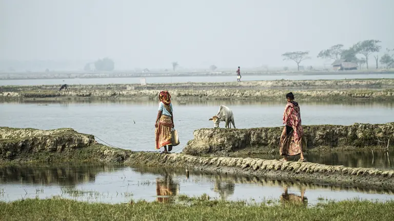 Two women walk along a ridge alongside an expanse of water.