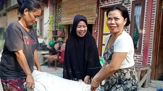 Three women holding a sack of rice between them.