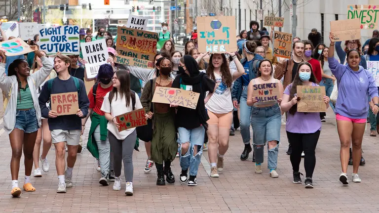 A group of young people, men and women, walk in line holding protest signs (saying things such as "fight for our future") as part of a march