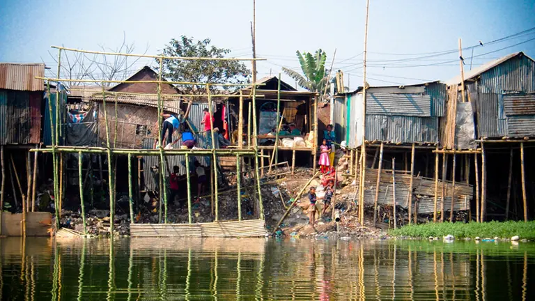 People building informal houses on stilts behind rising water.