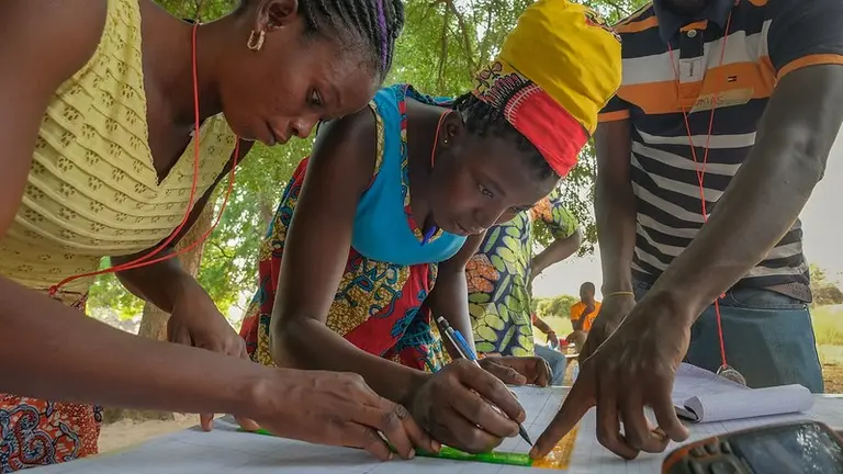 A woman holds a ruler on a piece of paper and another one draws with a pen.