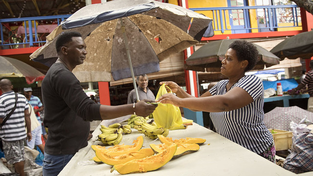 Woman stallholder selling bananas hands a bag to a man.